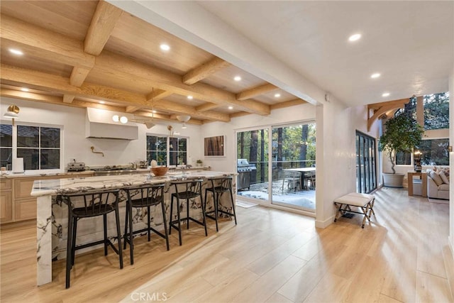 kitchen with light stone counters, beam ceiling, a large island, a breakfast bar area, and light hardwood / wood-style floors