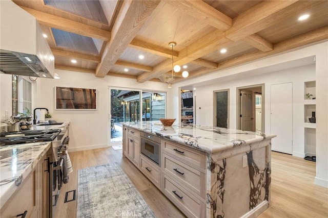 kitchen featuring appliances with stainless steel finishes, light stone countertops, light wood-type flooring, beam ceiling, and a spacious island