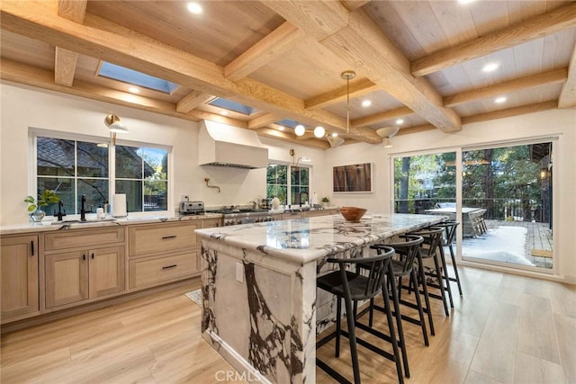 kitchen featuring sink, a center island, light stone countertops, custom range hood, and light brown cabinets