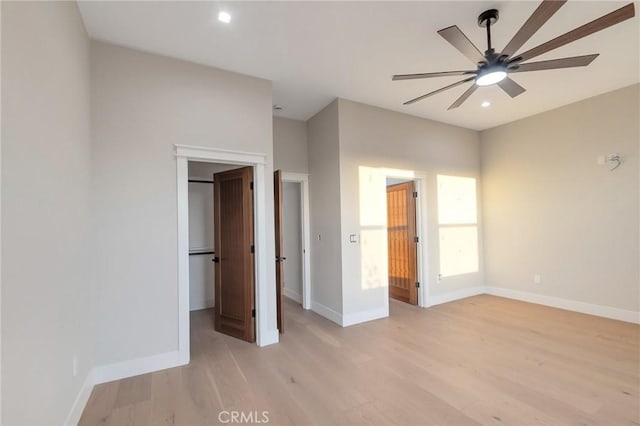 unfurnished bedroom with a walk in closet, ceiling fan, and light hardwood / wood-style flooring