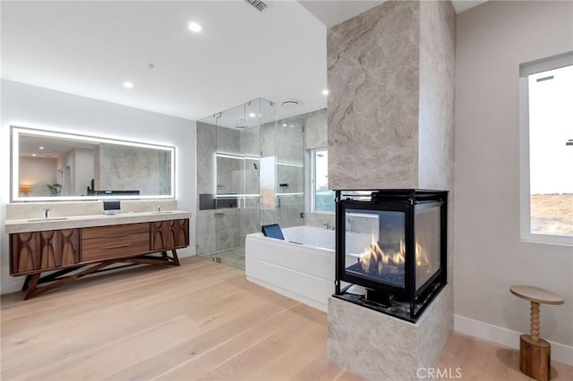 bathroom with a multi sided fireplace, wood-type flooring, plus walk in shower, and vanity