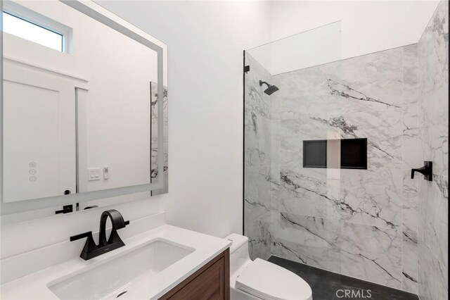 bathroom with tiled shower, vanity, and toilet