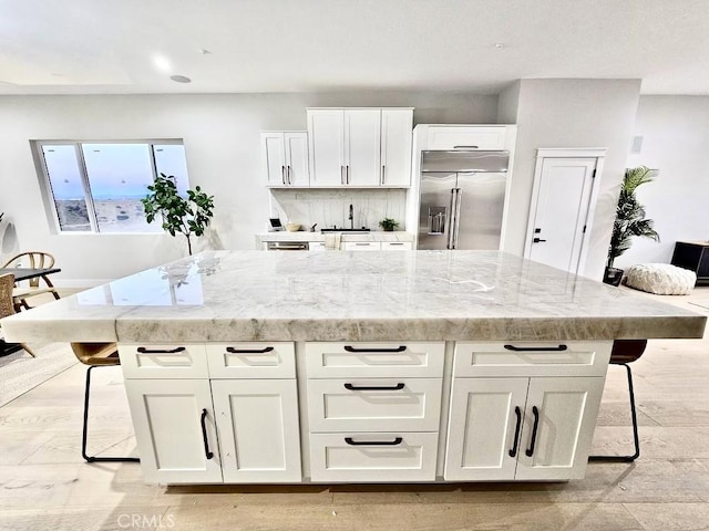 kitchen with white cabinetry, a breakfast bar, stainless steel built in fridge, and a kitchen island