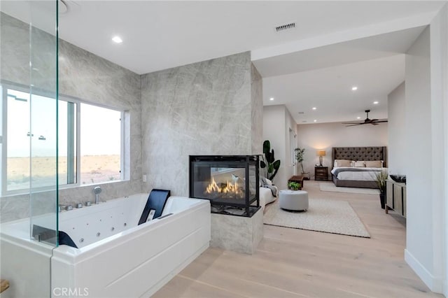 bathroom featuring a tub to relax in, wood-type flooring, a multi sided fireplace, and ceiling fan