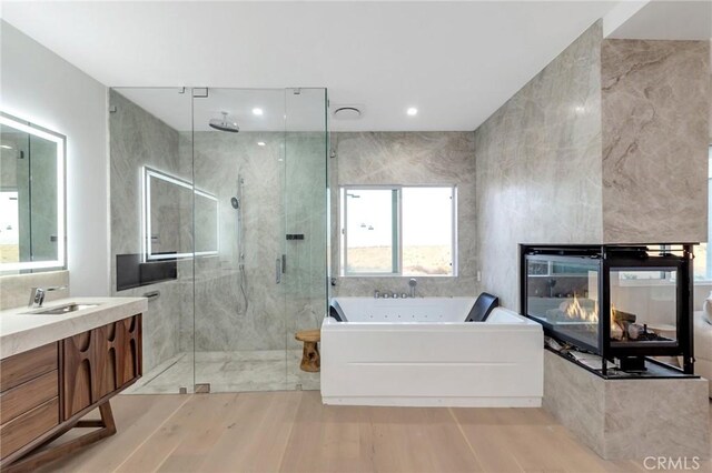 bathroom featuring shower with separate bathtub, a multi sided fireplace, hardwood / wood-style flooring, and vanity