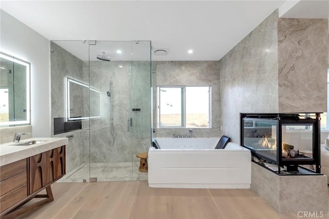 bathroom featuring wood-type flooring, tile walls, a multi sided fireplace, vanity, and plus walk in shower