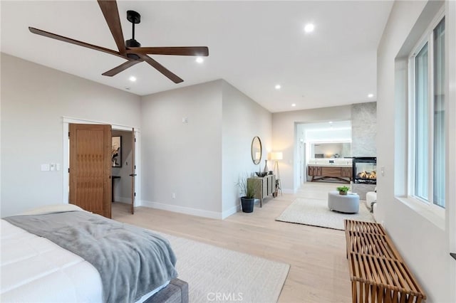 bedroom with ceiling fan, a multi sided fireplace, and light hardwood / wood-style floors