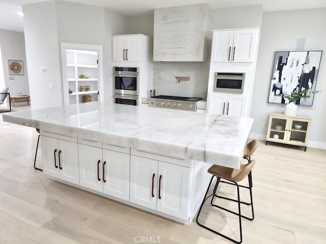 kitchen featuring light stone counters, light hardwood / wood-style floors, white cabinets, appliances with stainless steel finishes, and a spacious island