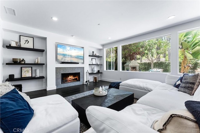 living room with recessed lighting, a warm lit fireplace, visible vents, and wood finished floors