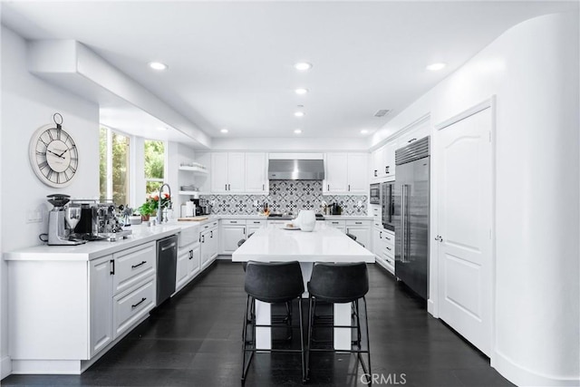 kitchen featuring a breakfast bar, appliances with stainless steel finishes, white cabinets, a sink, and wall chimney range hood