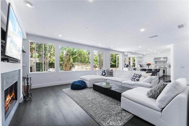 living area with a wealth of natural light, dark wood finished floors, visible vents, and a high end fireplace