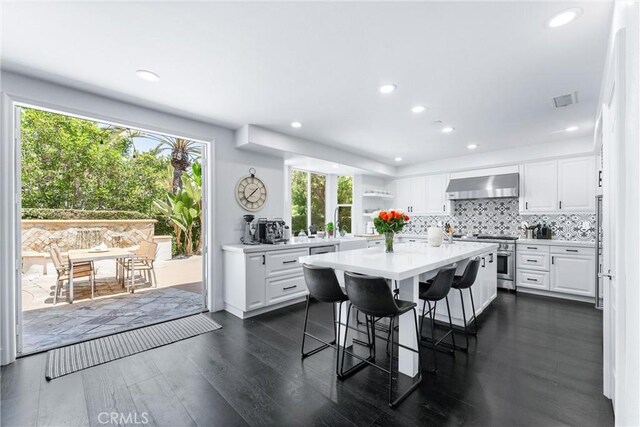 kitchen featuring a breakfast bar, white cabinetry, high end stainless steel range oven, and wall chimney exhaust hood