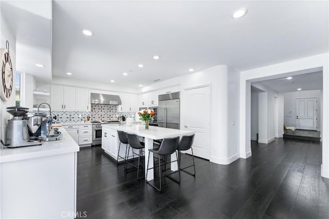 kitchen featuring a breakfast bar, high end appliances, backsplash, white cabinets, and wall chimney range hood