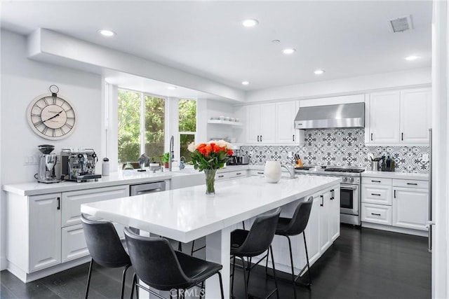 kitchen with wall chimney exhaust hood, appliances with stainless steel finishes, a breakfast bar, and white cabinetry