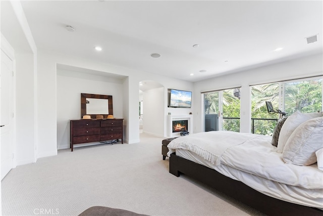 bedroom with a warm lit fireplace, baseboards, visible vents, and light colored carpet