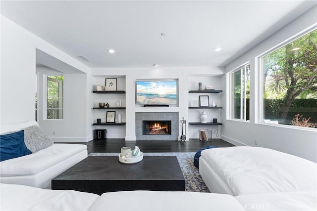 living area featuring a warm lit fireplace, recessed lighting, wood finished floors, and built in features