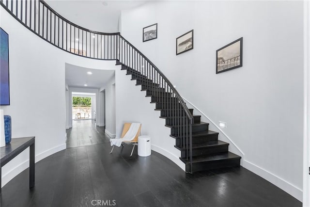 staircase featuring a high ceiling, baseboards, wood finished floors, and recessed lighting