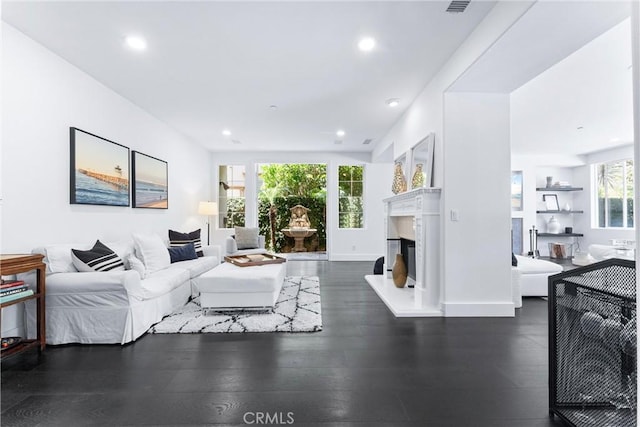 living area featuring baseboards, a fireplace with raised hearth, wood finished floors, and recessed lighting