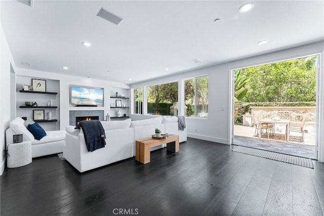 living area with dark wood-style floors, a warm lit fireplace, and recessed lighting