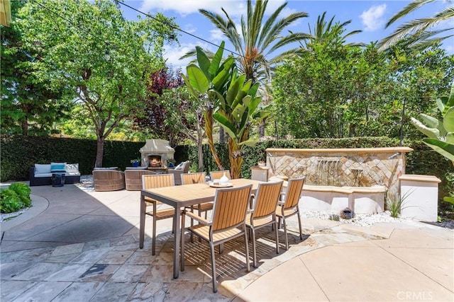 view of patio / terrace with a lit fireplace, fence, and outdoor dining space