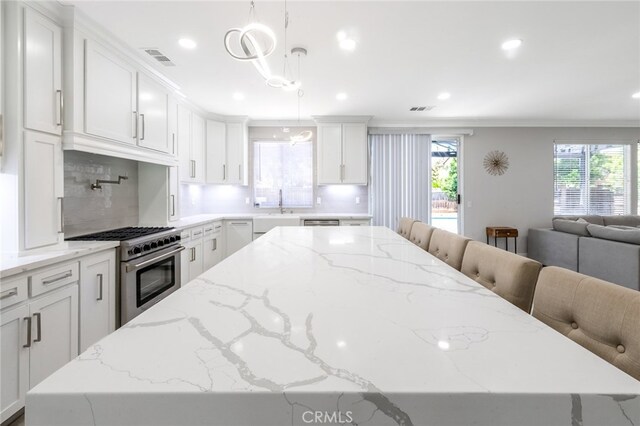 kitchen featuring high end stove, decorative backsplash, a kitchen breakfast bar, a center island, and pendant lighting