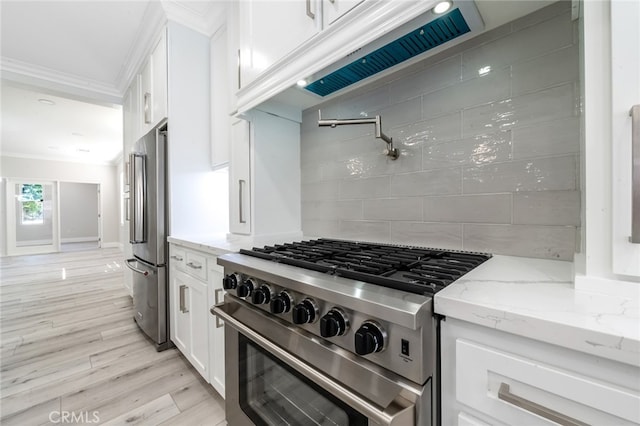 kitchen with premium appliances, light stone countertops, tasteful backsplash, white cabinetry, and light hardwood / wood-style flooring