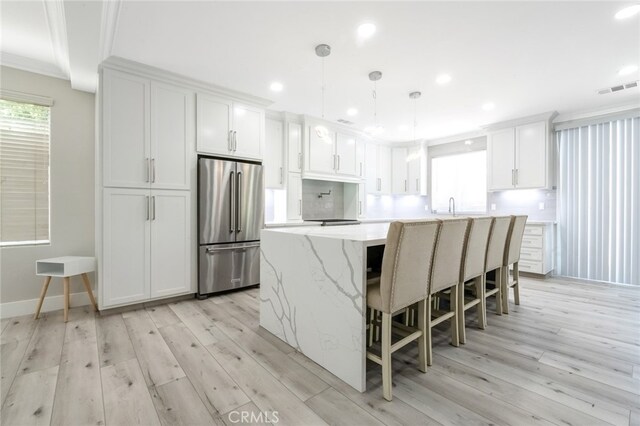 kitchen featuring high end refrigerator, a kitchen island, pendant lighting, white cabinets, and light hardwood / wood-style floors