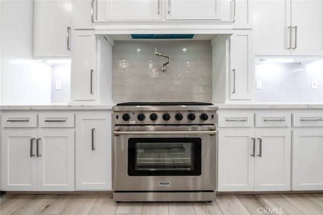 kitchen with light stone countertops, high end stainless steel range, white cabinets, and light hardwood / wood-style floors