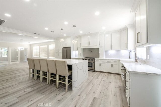 kitchen with sink, a center island, light wood-type flooring, premium appliances, and white cabinetry