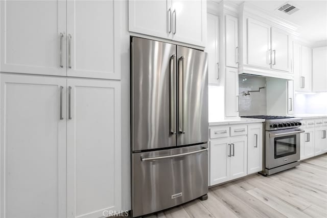 kitchen featuring high end appliances, crown molding, white cabinetry, and light wood-type flooring