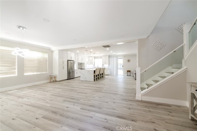 unfurnished living room with ornamental molding, light hardwood / wood-style flooring, and an inviting chandelier