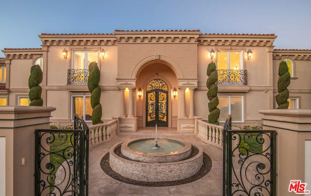 exterior entry at dusk featuring a balcony and french doors