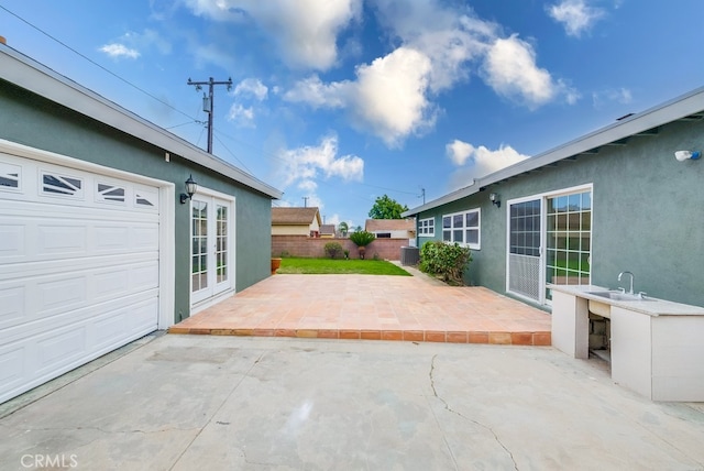 view of patio featuring central air condition unit, sink, french doors, and a garage