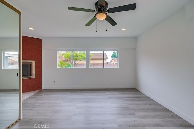 empty room with ceiling fan, a fireplace, and light hardwood / wood-style floors