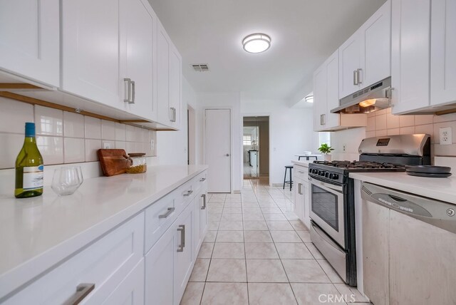 kitchen featuring decorative backsplash, white cabinetry, light tile patterned floors, and appliances with stainless steel finishes