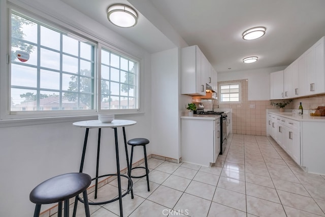 kitchen featuring white cabinetry, tile walls, gas range gas stove, and light tile patterned flooring