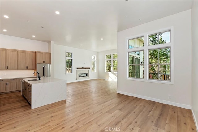 kitchen featuring sink, a center island with sink, light wood-type flooring, stainless steel appliances, and light stone countertops