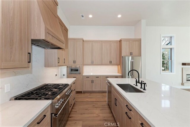 kitchen featuring light stone countertops, light brown cabinets, sink, light wood-type flooring, and high quality appliances