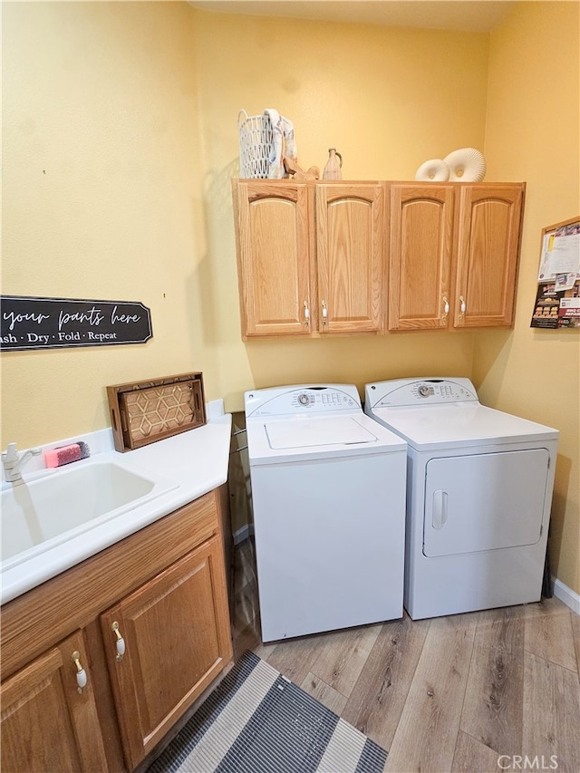 clothes washing area with washer and dryer, light hardwood / wood-style flooring, cabinets, and sink