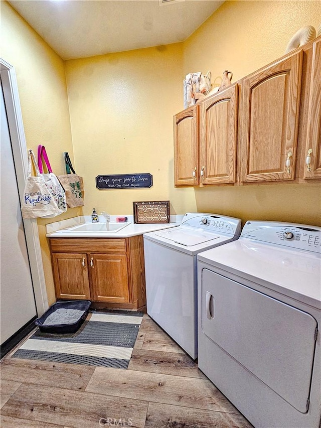 clothes washing area featuring separate washer and dryer, sink, cabinets, and light hardwood / wood-style flooring