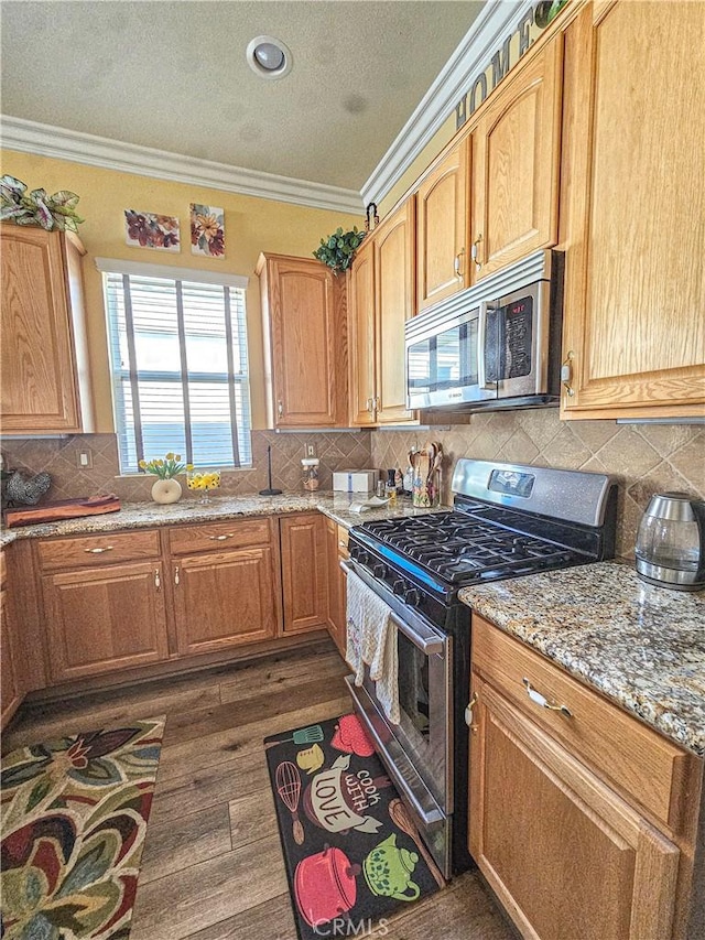 kitchen featuring dark wood-style flooring, a textured ceiling, crown molding, stainless steel appliances, and light stone counters
