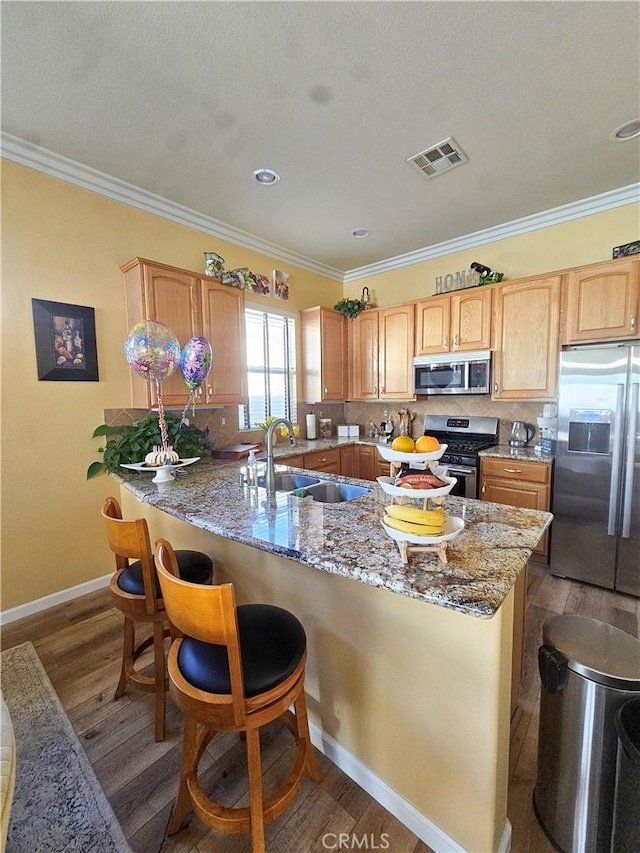 kitchen featuring ornamental molding, light stone countertops, appliances with stainless steel finishes, a sink, and wood finished floors