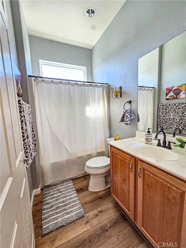 bathroom featuring toilet, wood finished floors, vanity, and shower / bath combo with shower curtain