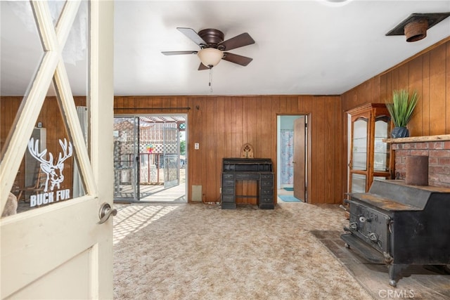 carpeted living area with a wood stove, wood walls, and ceiling fan