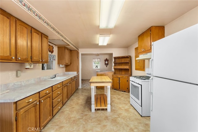 kitchen featuring brown cabinets, light floors, light countertops, white appliances, and under cabinet range hood