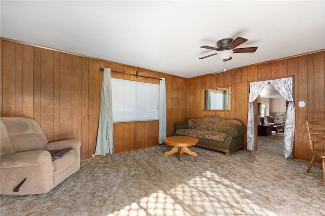 living area featuring carpet floors, ceiling fan, and wooden walls