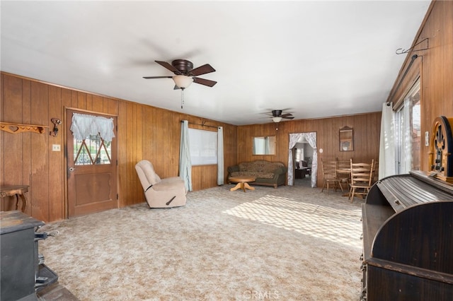 carpeted living area with a wood stove, ceiling fan, and wooden walls