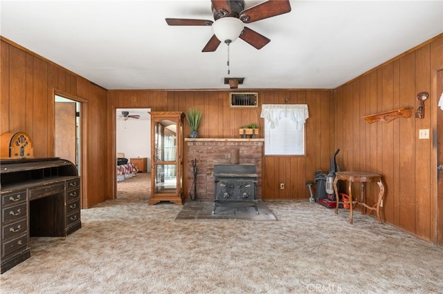 carpeted living area featuring visible vents, wood walls, a wood stove, and a ceiling fan