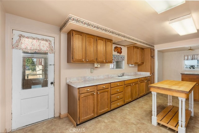 kitchen with baseboards, brown cabinetry, a sink, and light countertops