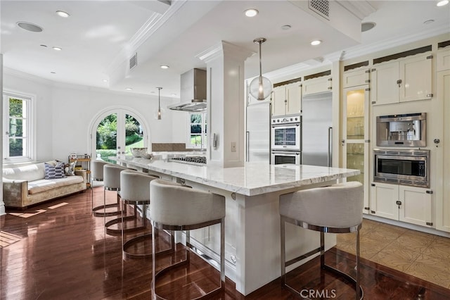 kitchen with wall chimney range hood, a breakfast bar, light stone countertops, decorative light fixtures, and dark hardwood / wood-style flooring